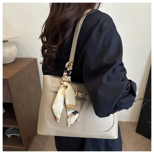 Beige tote bag with silk scarf detail and decorative buckle shown on shoulder