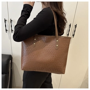 Detail of brown woven tote bag showing texture, slim straps and golden rivets on shoulder