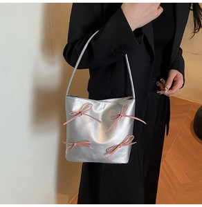 Detail of silver metallic tote bag featuring pink ribbons and leather texture on a model