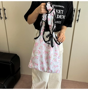 Close-up of floral tote bag with pink rose print, black ruffled trim and satin bow detail