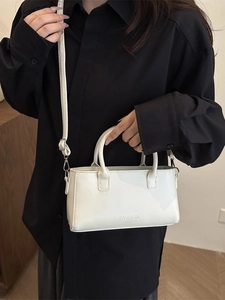 White rectangular leather handbag with FASHION embossing worn on black shirt
