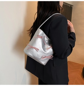 Silver metallic shoulder bag with pink bow detail worn by model for size reference