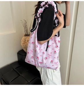 Pink floral tote bag with black ruffle straps shown on model in a modern room