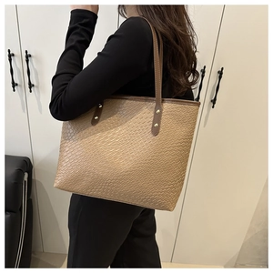 Detailed view of khaki crocodile pattern tote bag with brown straps and gold rivets