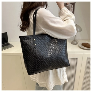 Detail of black woven tote bag featuring soft luster finish and golden metallic rivets