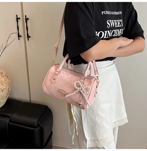 Detailed shot of pink snake texture Boston bag with pearl bow and heart pendant charm