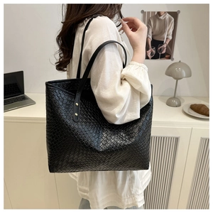 Détail d'un sac cabas tressé noir avec fines bandoulières et rivets dorés en décor intérieur