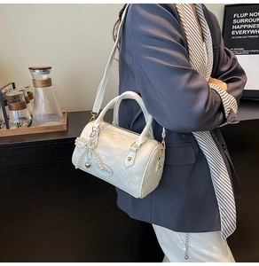 Detail of white Boston bag with snake texture, pearl bow charm, and gold heart pendant