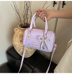 Detail view of lavender Boston bag with scale texture, pearl bow and gold hardware