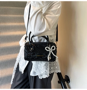 Close-up of black snake-pattern Boston bag with a pearl bow charm on the side