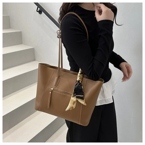 Close-up of brown tote bag with white stitching, outer pocket and decorative scarf