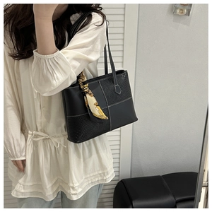 Detail of black crocodile pattern tote bag with decorative scarf on model
