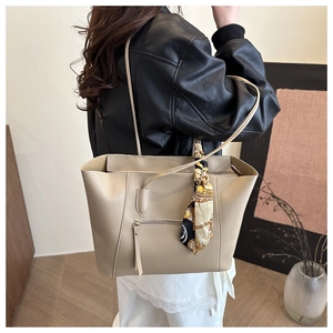Detailed view of beige tote bag with decorative silk scarf handle on a model's shoulder