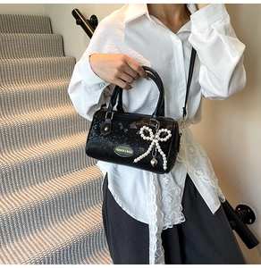 Détail d'un sac à main noir en cuir de serpent avec nœud perlé et accessoires dorés