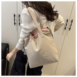 Detail of beige drawstring bucket bag with pink inner lining and black shoulder strap