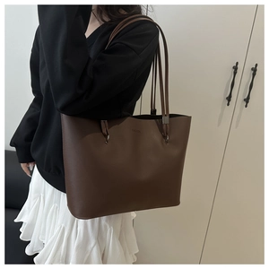 Close-up detail of dark brown leather tote bag with subtle fashion lettering