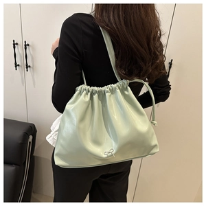 Détail du sac seau vert menthe à cordon avec nœud argenté porté par le modèle