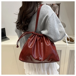 Dettaglio borsa a secchiello bordeaux lucida con fiocco bianco e sottile tracolla da donna