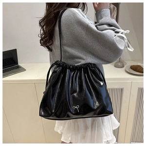 Close-up of black glossy drawstring bucket bag with silver metal bow detail in setting