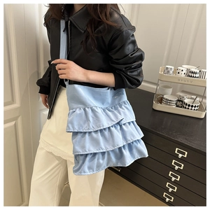 Model wearing a light blue layered ruffle tote bag with wide strap in a modern room