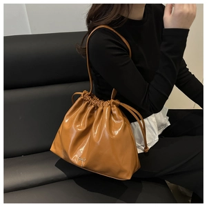 Detail of caramel brown glossy patent leather bucket bag with silver bow accent