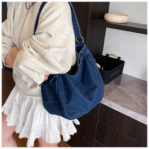 Dettaglio della borsa hobo in denim blu scuro con cuciture bianche e tracolla larga
