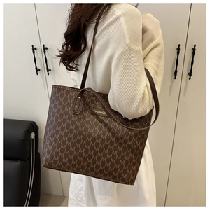 Detail of brown tote bag with repeating M patterns and gold fashion emblem