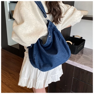 Detail of blue denim hobo bag showing contrast stitching and metal snap closure
