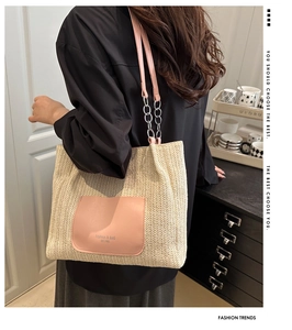 Detail of woven straw tote bag with pink leather pocket and chain strap on shoulder