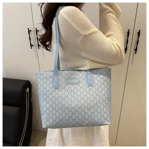 Detail of light blue tote bag with M-pattern print and gold Fashion brand plate