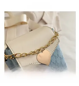 Detalle de bolso mini cuadrado con colgante de corazón, cadena dorada y patrón de jacquard