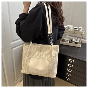 Modellansicht einer großen cremefarbenen Strohtasche mit Ledertasche und Kettengurt