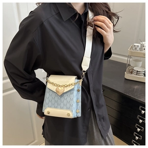 Detail of light blue crossbody bag with white M-pattern, gold heart charm, and wide strap