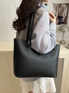 Minimalist large black tote bag in matte leather worn by a model in a cozy indoor setting