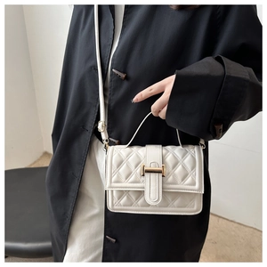Detail der cremefarbenen Stepptasche mit goldener Schnalle am dunklen Mantelmodell