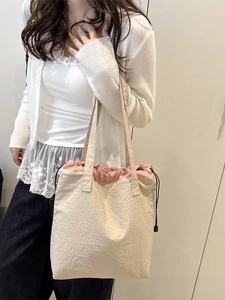 Large beige canvas tote bag with pink drawstring closure for women on a female model
