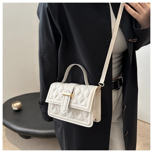 Detail einer weißen Stepphandtasche mit goldener Metallschnalle und Lederstruktur