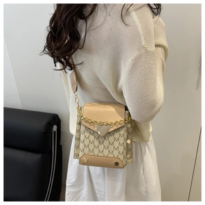 Detail of beige crossbody bag with M-pattern texture, golden chain and heart charm