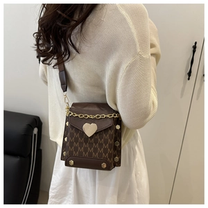 Detail of brown mini crossbody bag with M-pattern print, heart buckle and gold rivets