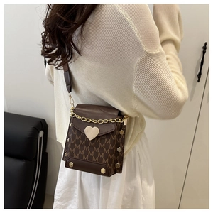 Detail of a brown crossbody bag with heart lock and chain, shown worn by a model