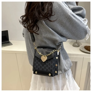 Macro detail of black crossbody bag with gold chain heart pendant and floral print