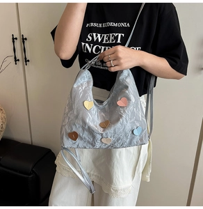 Detail der silbernen Metallic-Tasche mit bunten Lederherzen und schmalem Schultergurt