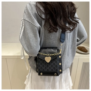 Detalle del bolso bandolera negro con cierre de corazón dorado y estampado M en correa