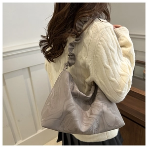 Detail der Schultertasche mit Marmormuster und Rüschenriemen über creme Strickpullover