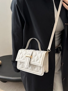 Elegante cremefarbene Stepphandtasche mit goldener T-Schließe getragen zum schwarzen Blazer