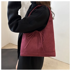 Detail of burgundy suede tote bag with drawstring bow on model in minimalist interior