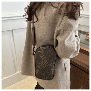 Detail of dark brown leather crossbody bag with letter print and adjustable strap