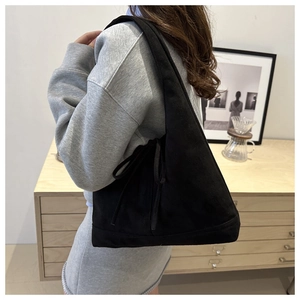 Detail of drawstring bow on black suede tote bag shown on model in modern setting