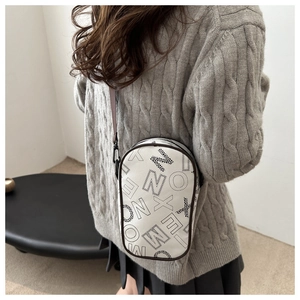 Vertical white leather crossbody bag with black letter prints worn with a grey knit sweater