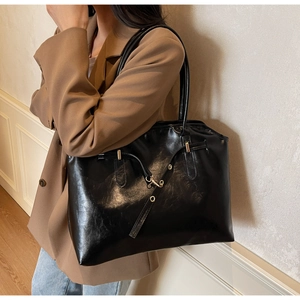 Close-up of a black glossy large tote bag with metallic buckle detail and PU leather texture